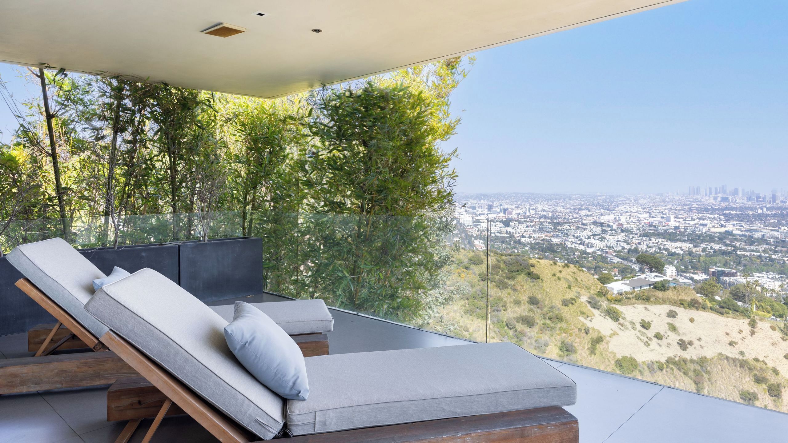 A modern outdoor lounge with a city view, featuring a glass barrier, wooden flooring, and a minimalist design.
