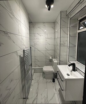 A modern bathroom with marble walls and floor, a toilet, a sink, and a mirror.