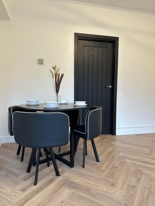 A dining area with a black table and chairs, a vase with dried plants, and a door in the background.