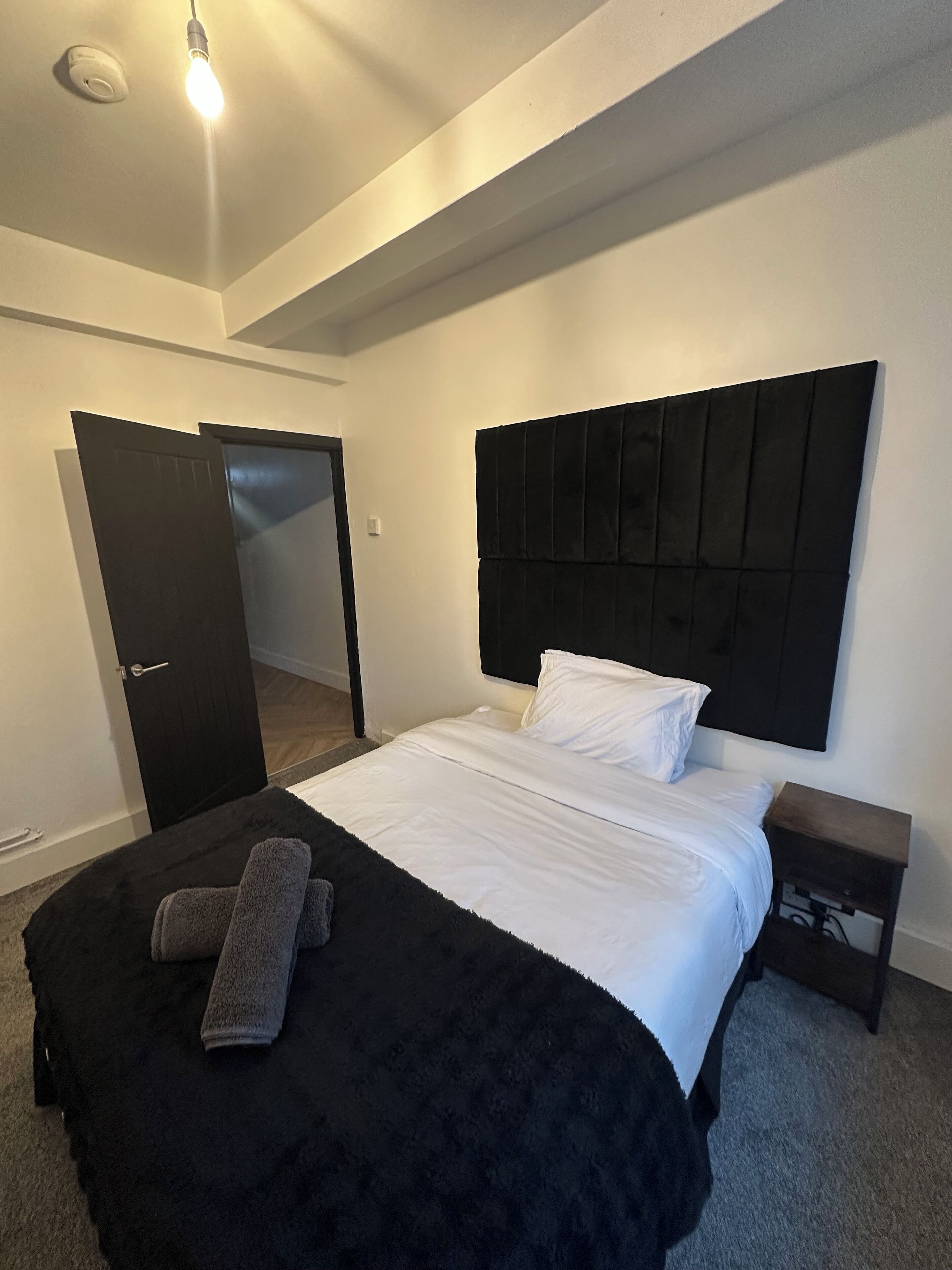A bedroom with a bed, a black headboard, a bedside table, and a door.