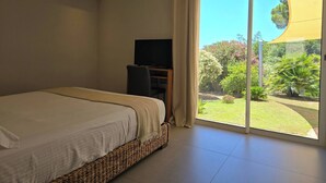 Une chambre à coucher avec un lit, une télévision et une vue sur un jardin, accessible par une porte coulissante.