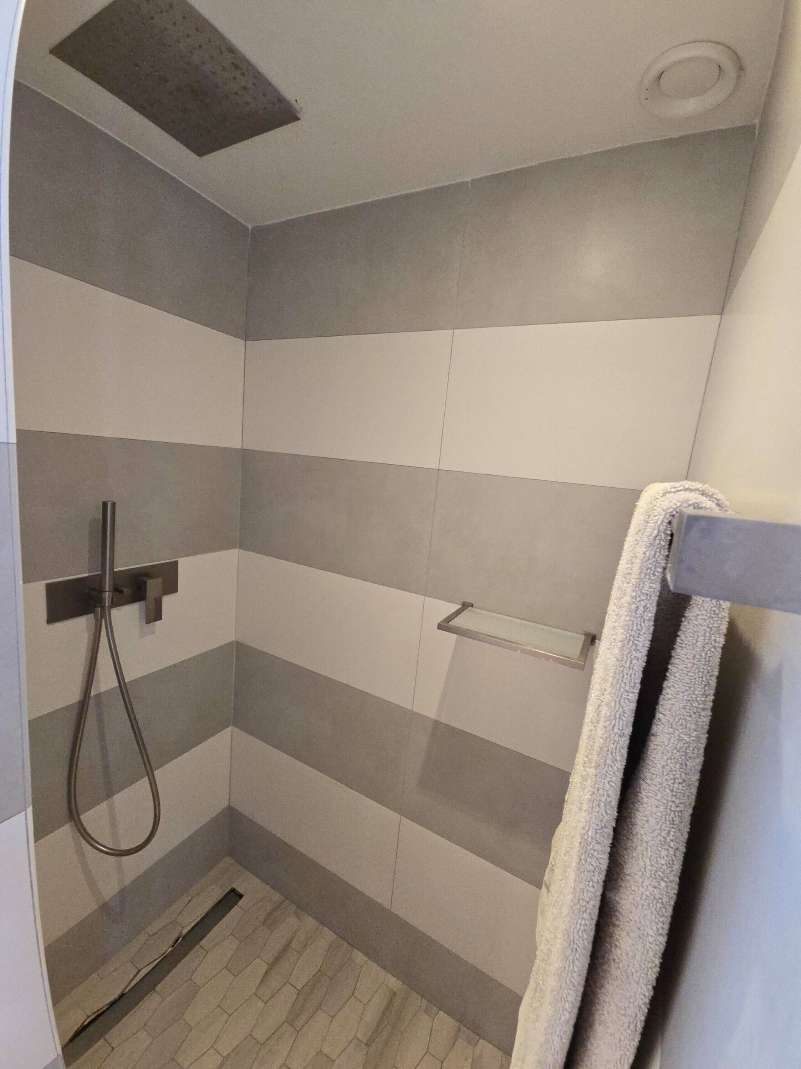 A shower with a handheld showerhead and a towel rack.