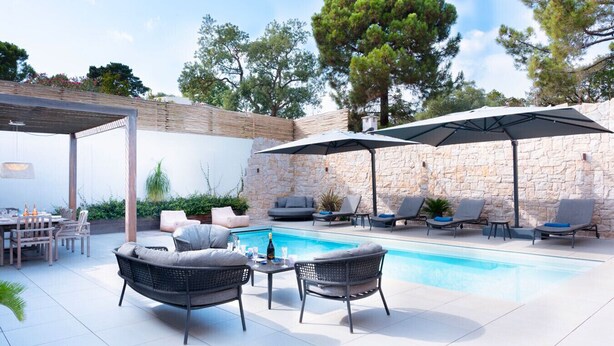 Un espace extérieur avec une piscine, des chaises longues, une table à manger et des parasols.