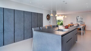 Une cuisine moderne dotée d’un grand îlot central, de luminaires suspendus et d’un coin repas avec une table et des chaises.