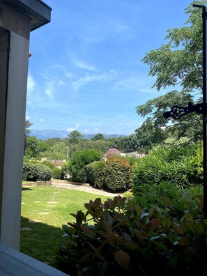 A garden with a lawn, various shrubs, and a view of distant mountains under a clear sky.