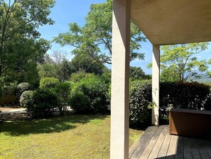 A covered outdoor area with a wooden deck, surrounded by lush greenery and trees.
