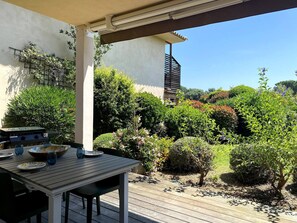 An outdoor patio with a wooden table and chairs, surrounded by lush greenery and a clear blue sky. - T3 face à la Mer by Pinarello Villa Services (Sainte-Lucie de Porto-Vecchio)