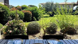A patio table with two plates and two glasses, surrounded by a garden with various plants and a view of a house in the background. - T3 face à la Mer by Pinarello Villa Services (Sainte-Lucie de Porto-Vecchio)