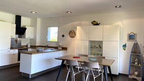 A modern kitchen with white cabinetry, a central island, and a dining area with chairs. - T3 face à la Mer by Pinarello Villa Services (Sainte-Lucie de Porto-Vecchio)