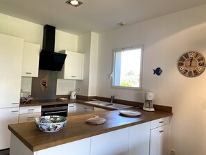 Une cuisine moderne avec des armoires blanches, une hotte noire, une fenêtre et une horloge en bois accrochée au mur.