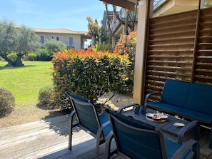Une terrasse extérieure avec une table et deux chaises, une terrasse en bois et une vue sur un bâtiment et un jardin.