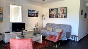 A modern living room with a grey sofa, a pink chair, a flat-screen TV, and artwork on the walls. - T3 face à la Mer by Pinarello Villa Services (Sainte-Lucie de Porto-Vecchio)