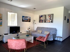 Un salon moderne avec un canapé gris, un fauteuil rose, un téléviseur à écran plat et des œuvres d’art accrochées aux murs.