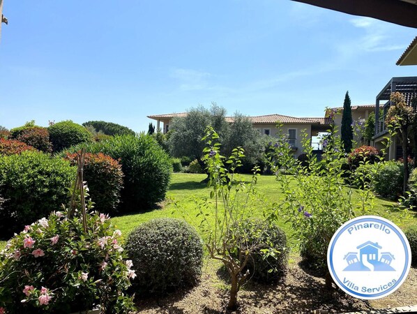 A villa with a well-maintained garden, a clear blue sky, and a logo for Pinarello Villa Services.