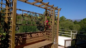 A wooden pergola with a bench, surrounded by lush greenery and a clear view of distant mountains.