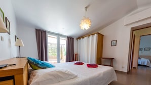 A bedroom with a large bed, a desk, a lamp, and a view of the outside.