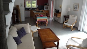 A living room with a sofa, chairs, a dining table, and a kitchen area with a microwave and stove.
