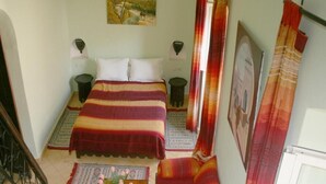 A bedroom with a bed, two bedside tables, a nightstand, a window with curtains, and a painting on the wall. - RIAD in the heart of the medina, 3 minutes from the beach (Essaouira)