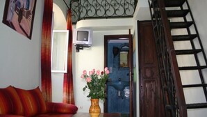 A living room with a sofa, a table, a vase with flowers, a television, and a staircase. - RIAD in the heart of the medina, 3 minutes from the beach (Essaouira)