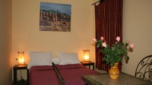 A hotel room with a bed, two bedside tables with lamps, a table with a vase of flowers, and a painting on the wall. - RIAD in the heart of the medina, 3 minutes from the beach (Essaouira)