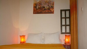 A bed with a striped blanket, two bedside lamps, a painting on the wall, and a window with curtains. - RIAD in the heart of the medina, 3 minutes from the beach (Essaouira)