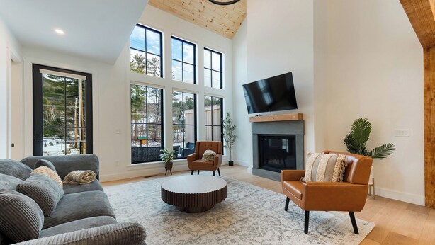 A spacious living room with a large window, a fireplace, and a flat-screen TV mounted above it. - Brand NEW Ski-in/Ski-out retreat at Cranmore Mt.! (North Conway)