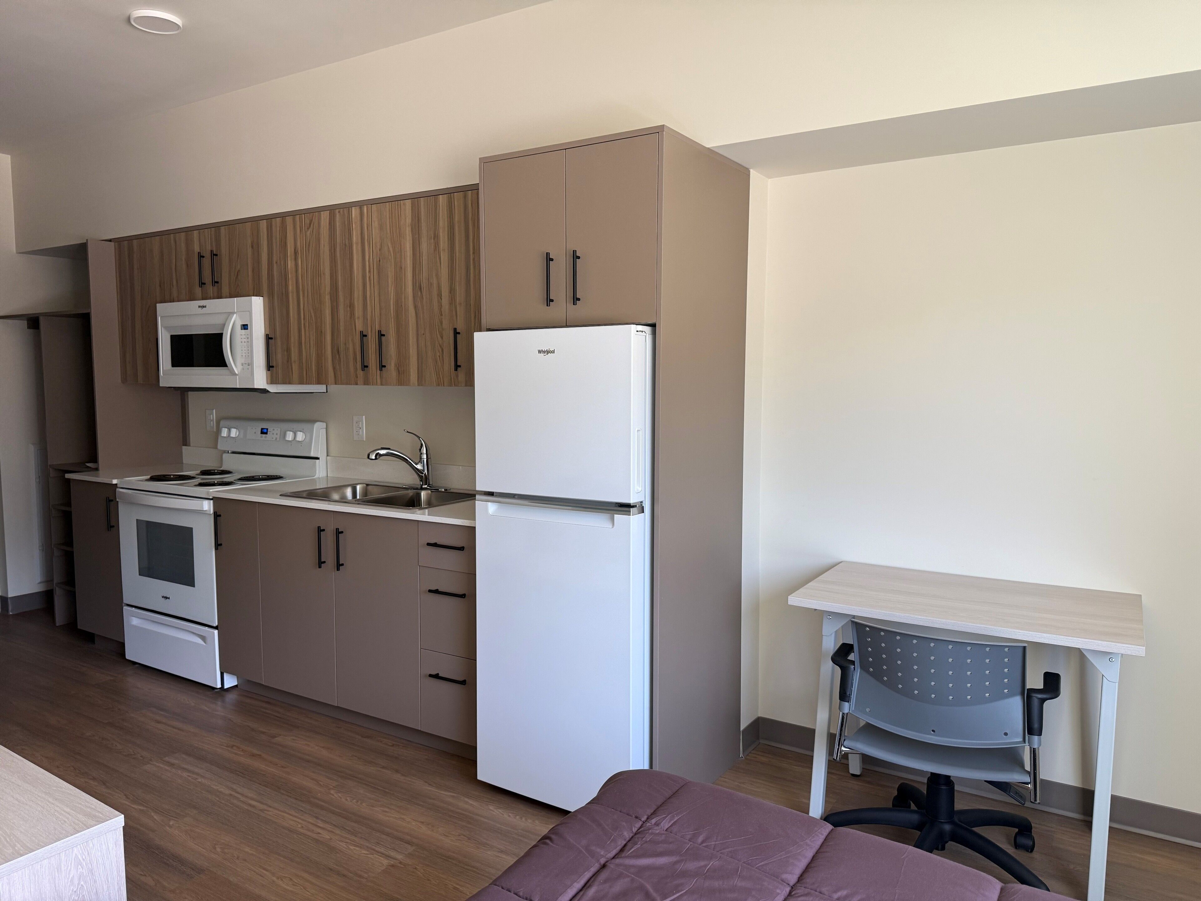 A modern kitchen with a microwave, stove, refrigerator, and wooden cabinets.
