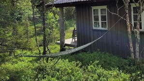 Uma cabana rústica rodeada por uma floresta densa, com um alpendre de madeira e uma rede.