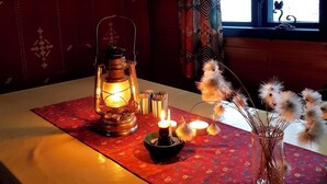 Um quarto com janela, mesa com lanterna, velas e flores secas.