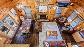A cozy cabin interior with a stone fireplace, wooden furniture, and a large window overlooking a scenic view.