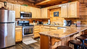 A wooden cabin-style kitchen with a stainless steel refrigerator, a microwave, an oven, and a sink.