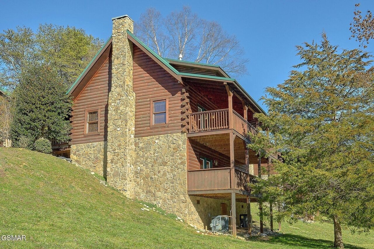 A log cabin with a stone foundation, a balcony, and a chimney.
