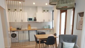 Ein modernes Wohnzimmer mit Sofa, Sessel und Couchtisch. Im Hintergrund ist ein Essbereich mit Tisch und Stühlen zu sehen.