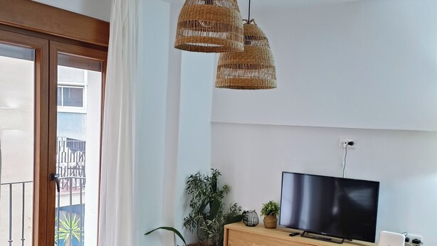 Ein modernes Wohnzimmer mit einer Couch, einem Sessel, einem Glastisch und einem Fernseher auf einem Holzschrank.
