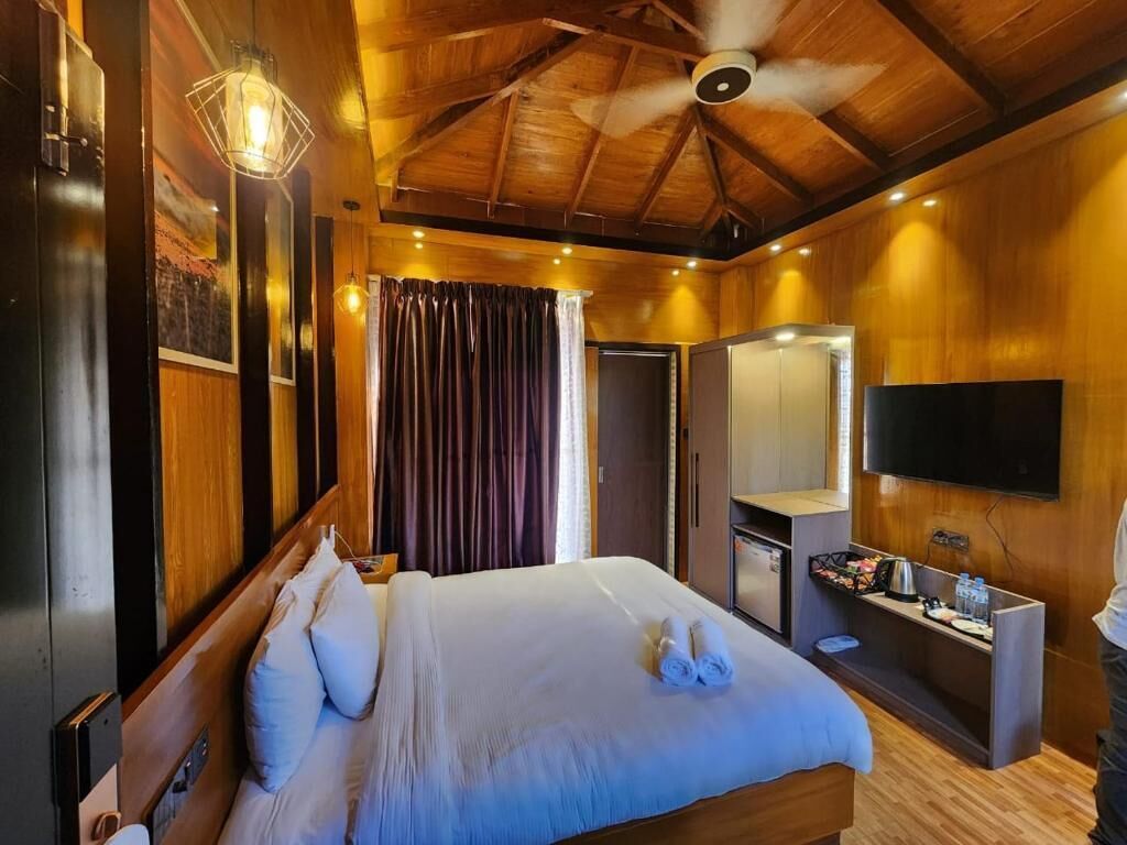 Un dormitorio bien iluminado con una cama grande, ventilador de techo, televisor y una pequeña zona de escritorio.