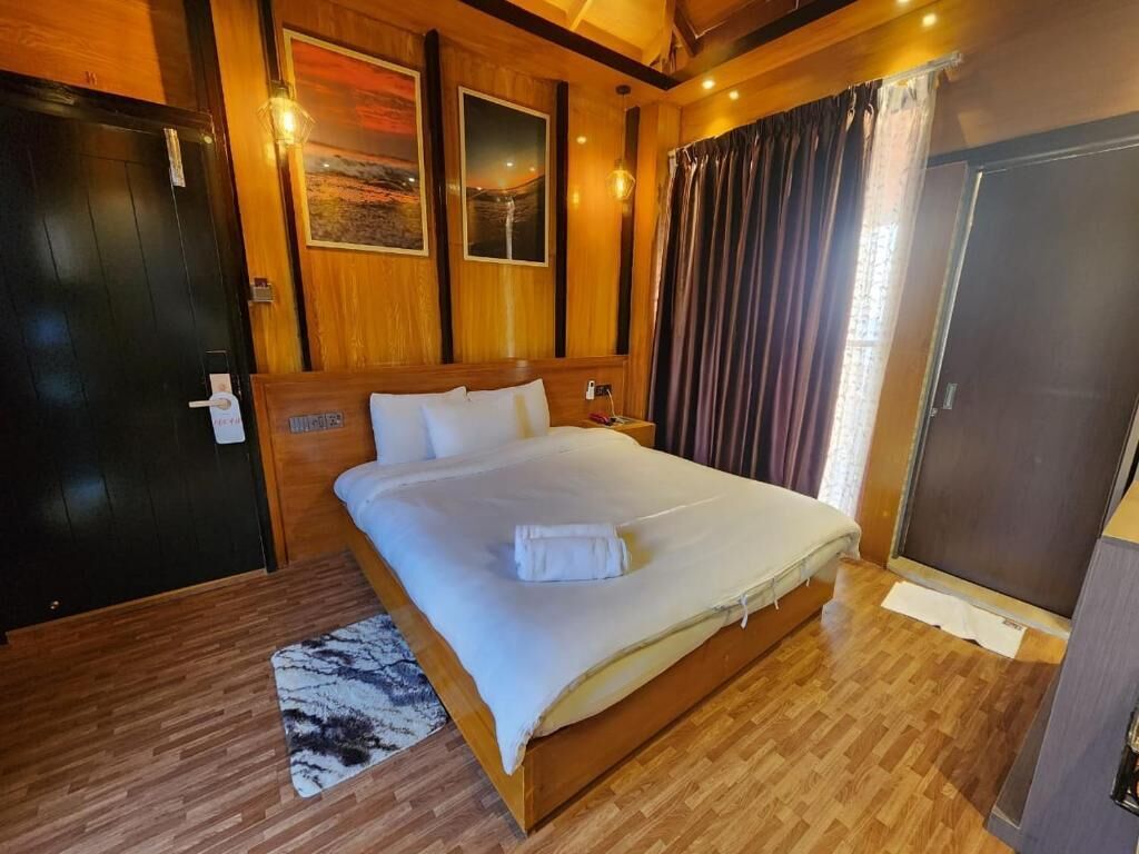 A wooden room with a bed, a door, and a painting on the wall.