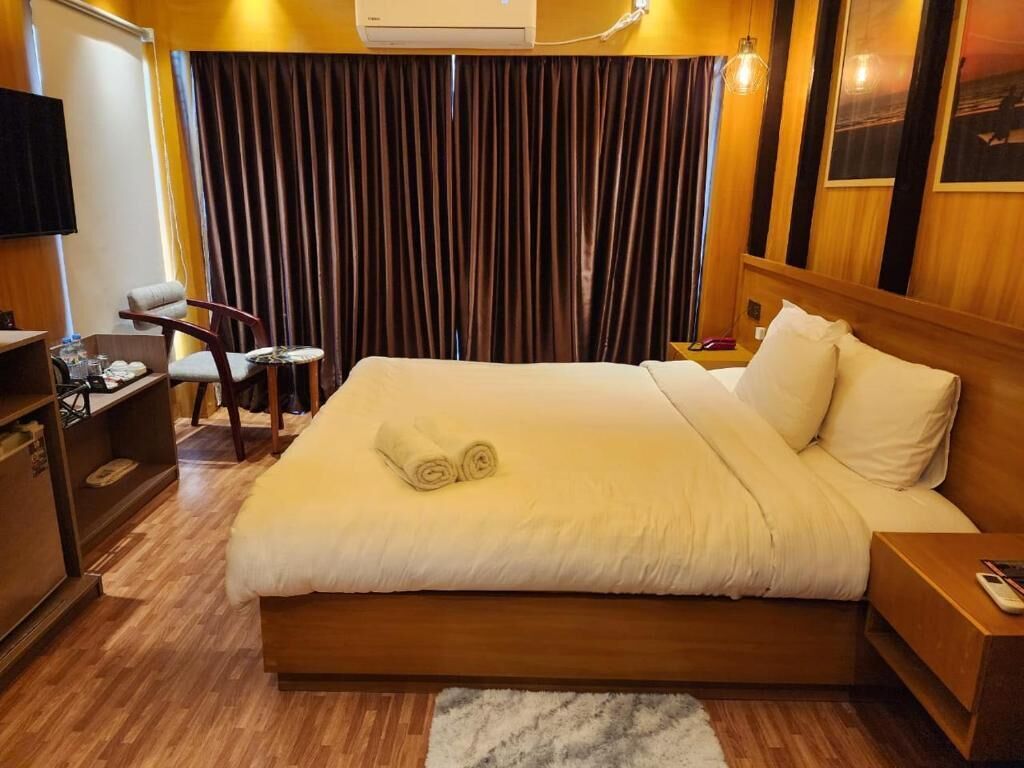 Une chambre d’hôtel avec un grand lit, une tête de lit en bois, un petit bureau, une chaise et un téléviseur fixé au mur.