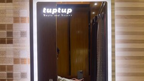 A bathroom with a large mirror, a sink with toiletries, and a sign reading "tuptup Resto and Resort". - TUPTUP - Resto & Resort (Cox's Bazar)