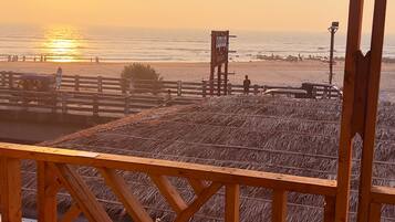A wooden deck with a view of the beach and ocean during sunset.