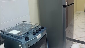A kitchen with a gas stove, a refrigerator, and tiled walls.