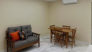A room with a sofa, a dining table with chairs, and an air conditioning unit on the wall.