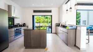 A modern kitchen with a central island, built-in oven, and a large window providing a view of greenery. - House Los Amigos 4 BR A/C - 9 persons / 2 minutes from beach / private pool Wifi (Las Terrenas)
