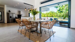 A modern kitchen with a built-in refrigerator, dining area with wicker chairs, and a large window overlooking a lush garden. - House Los Amigos 4 BR A/C - 9 persons / 2 minutes from beach / private pool Wifi (Las Terrenas)