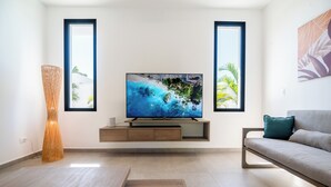 A modern living room with a flat-screen TV on a wooden stand, a sofa, and a large window with a view of a beach. - House Los Amigos 4 BR A/C - 9 persons / 2 minutes from beach / private pool Wifi (Las Terrenas)