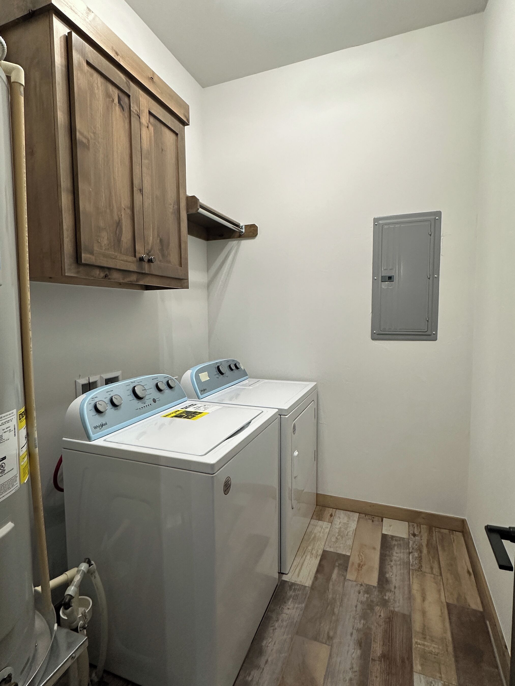 Une buanderie équipée d’un lave-linge et d’un sèche-linge à chargement frontal, de meubles en bois, d’un mur utilitaire et d’un sol carrelé.