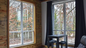 A cabin interior with large windows, a small table, and a leather chair. - Cozy, Rustic Cabin w/ Pool Table, Foosball, & Fast WiFi, South of Norman (Purcell)