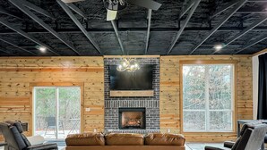 A cozy living room with a fireplace, leather sofas, and a large window offering a view of trees. - Cozy, Rustic Cabin w/ Pool Table, Foosball, & Fast WiFi, South of Norman (Purcell)