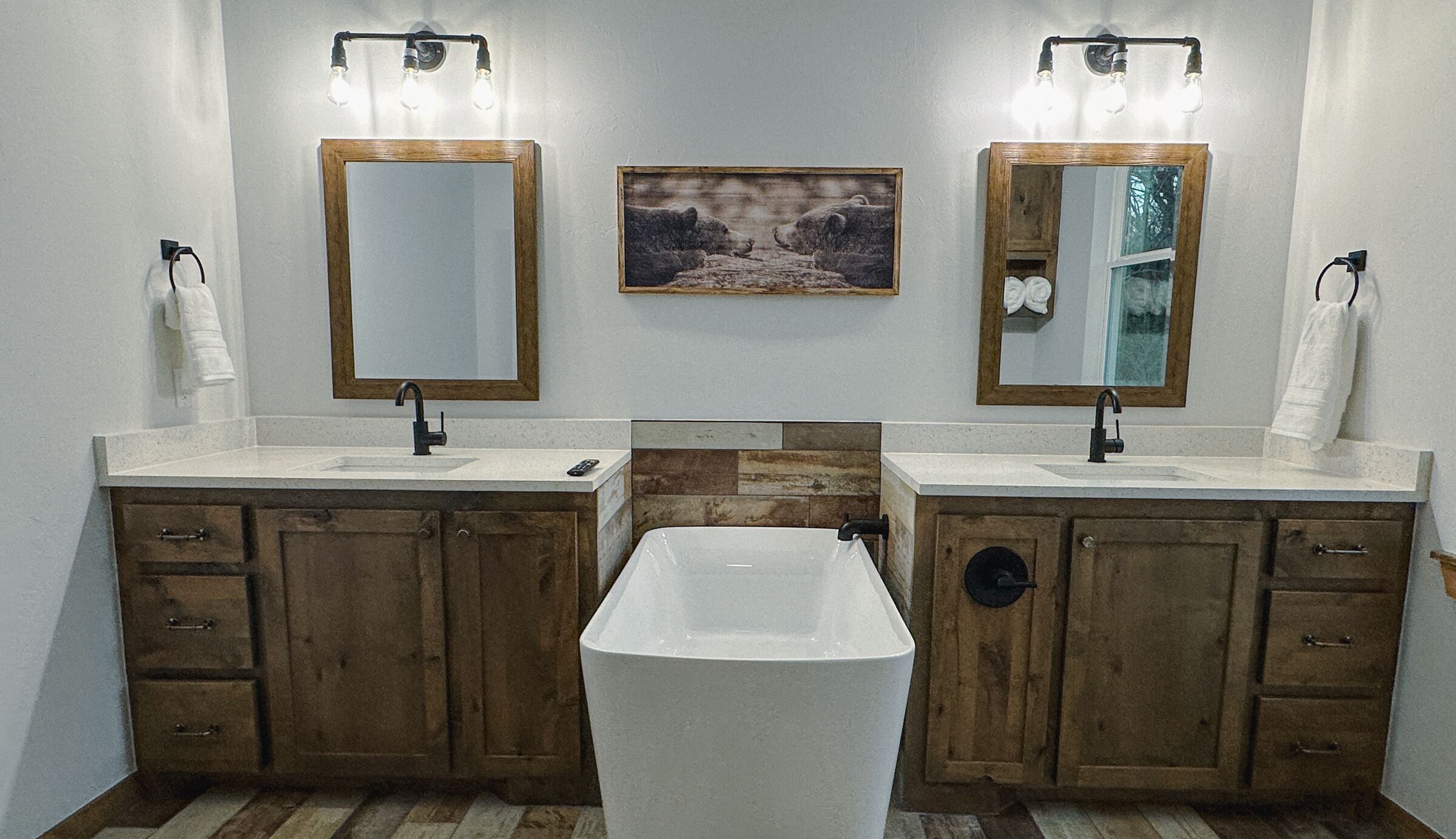 Un baño con dos lavamanos, armarios de madera, una bañera central e iluminación empotrada.