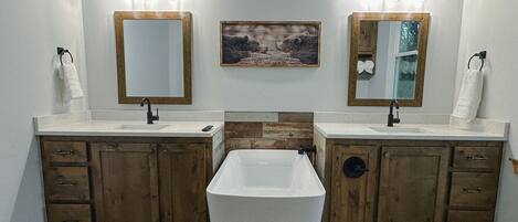 Un baño con dos lavamanos, armarios de madera, una bañera central e iluminación empotrada.