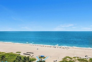 A beach with clear blue water, sandy shore, and umbrellas.